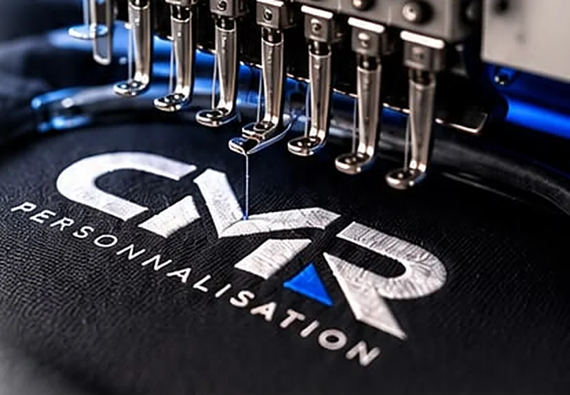 Machine à broder en train de réaliser le logo CMR Personnalisation sur un textile noir